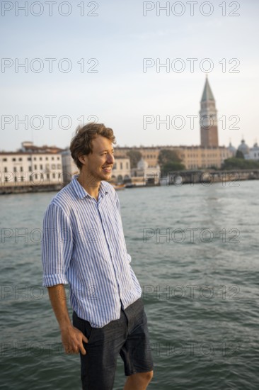 Young man in striped shirt and shorts on the banks of the Grand Canal, behind Campanile, Venice,