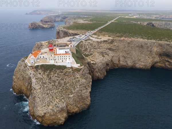A remote lighthouse and several buildings stand on a cliff, with a wide view of the ocean and the