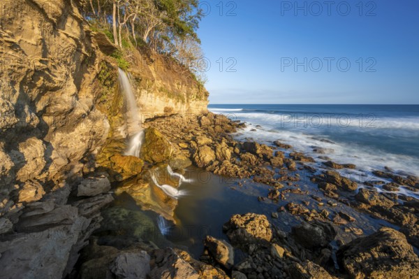 Waterfall falls into the sea on the cliffs, Catarata el Chorro, coastal landscape in the evening