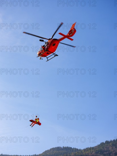 Injured person in a mountain bag with an air rescuer being winched into the rescue helicopter