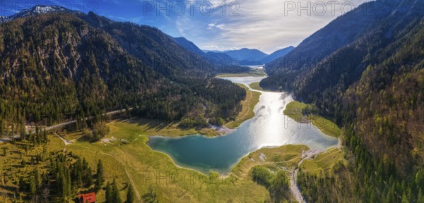 Mountain landscape with lake and forest, reflection of the sun in the water under a blue sky,