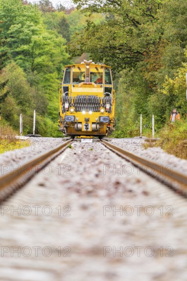 A yellow tractor unit drives directly towards the viewer, surrounded by autumnal forest, Hermann