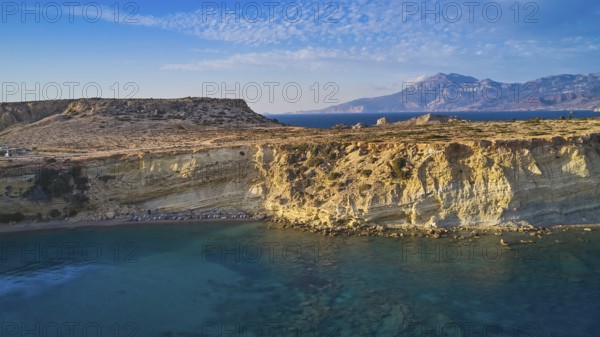 Rocky coast with bright sunshine and blue sky by the sea, drone shot, evening light, Paralia Agios