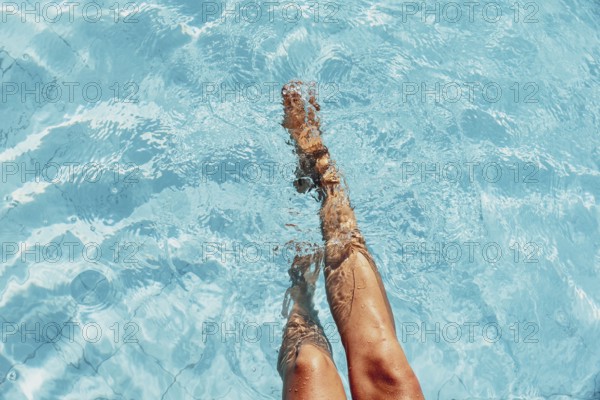 Two legs dipping in the sunny blue pool water, relaxed atmosphere