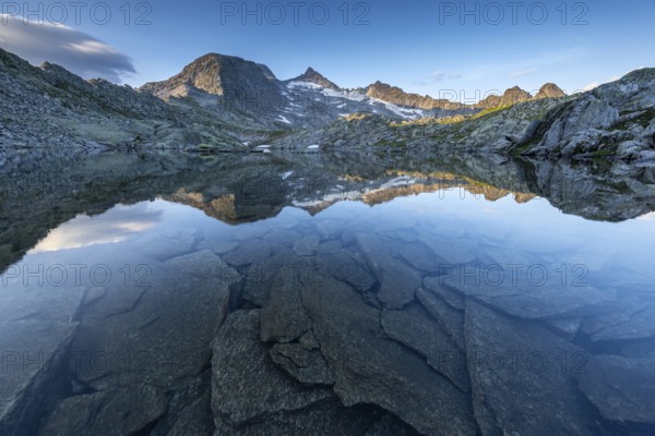 Mountain peaks and rocks reflected in the clear water of a lake at sunrise, Krimml, Salzburg,