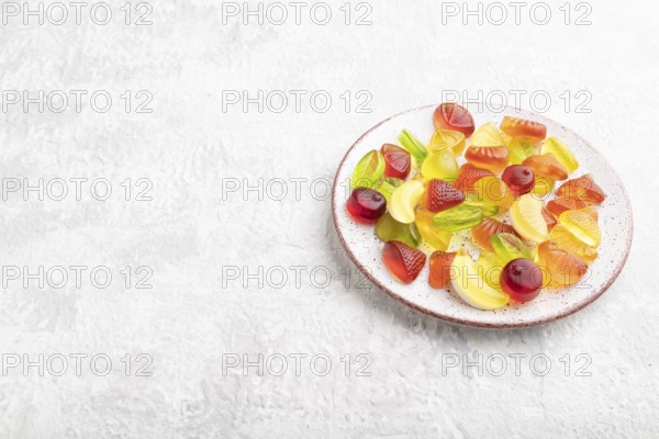 Various fruit jelly candies on plate on gray concrete background. side view, copy space