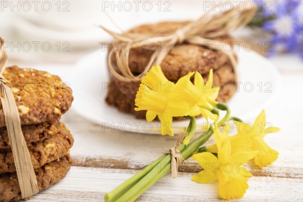 Oatmeal cookies with spring snowdrop flowers bluebells, narcissus and cup of coffee on white wooden