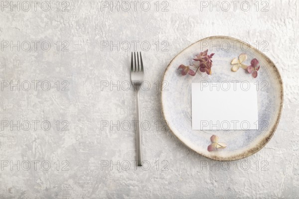White paper invitation card, mockup with dried hydrangea flowers on ceramic plate and gray concrete