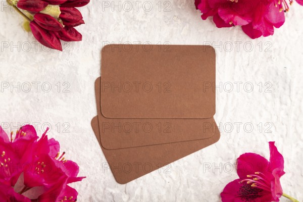 Brown business card with purple azalea flowers on gray concrete background. top view, flat lay,