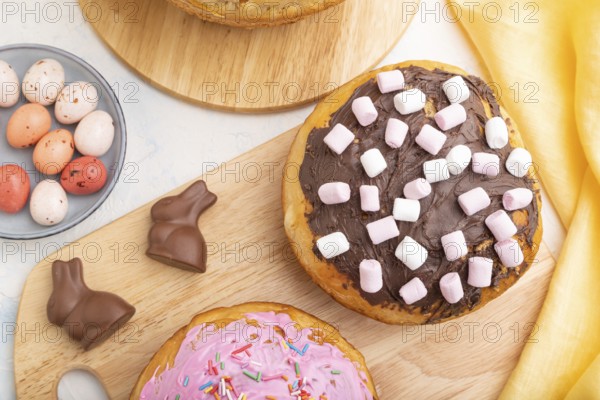Homemade glazed and decorated easter pies with chocolate eggs and rabbits on a white concrete