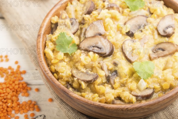 Lentils porridge with champignons and coriander in a wooden bowl on a white wooden background and