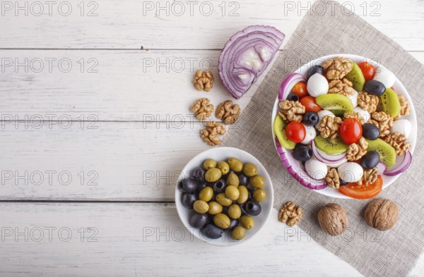 Salad with fresh cherry tomatoes, mozzarella cheese, olives, kiwi, onion and walnuts on white