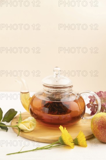 Red tea with herbs in glass teapot on white wooden background. Healthy drink concept. Top view,