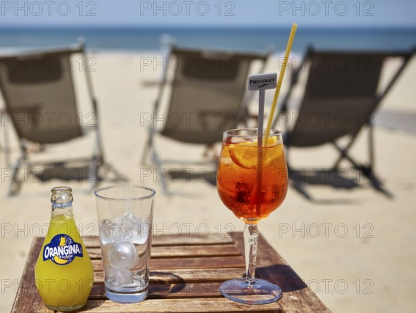 A bottle of Orangina, a glass with ice cube cubes and a glass of Aperol Spritz with a straw in a