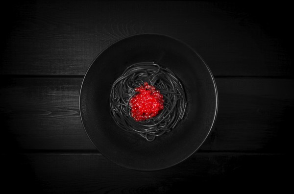 Black spaghetti with red caviar, pasta, on a black background, top view, no people