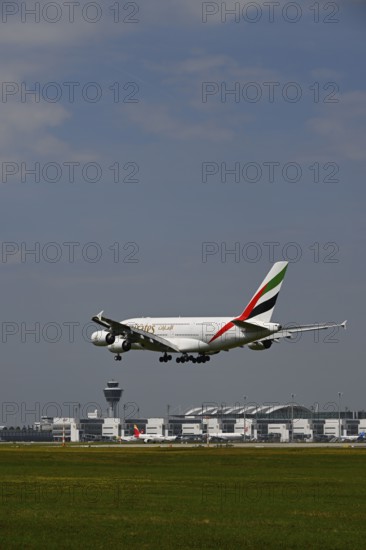 Emirates Airbus A380-800 approaching under blue sky, with control tower and Terminal 2 landing on