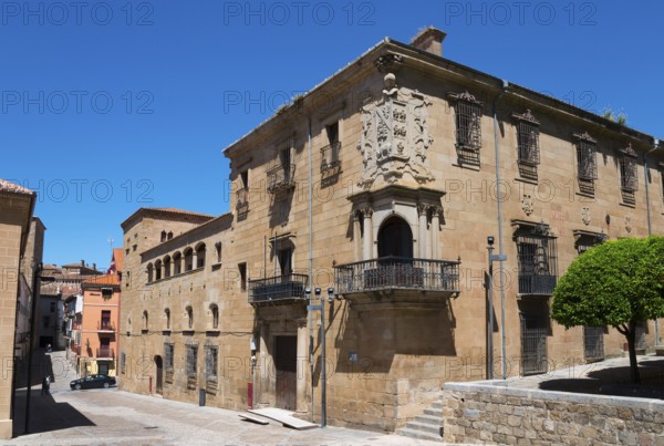 Historic sandstone city building with balcony and coat of arms under a clear sky, surrounded by