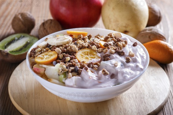 Vegetarian salad of bananas, apples, pears, kumquats, kiwi with granola and yogurt on brown woodem