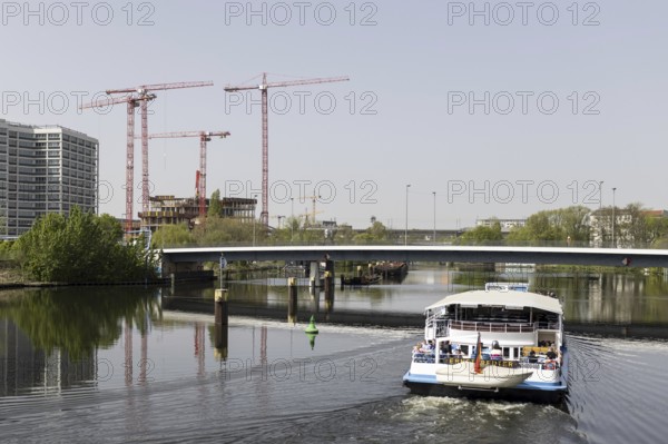 Four red construction cranes stand on a building site in Berlin's Heidestraße while a tourist boat
