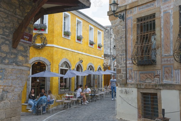 Busy people sitting in front of historic buildings under parasols in an old town alley, Xanthi,