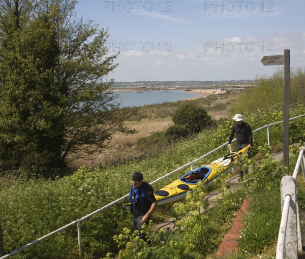 Two men carrying a canoe down to the beach, West Mersea, Mersea Island, Essex, England, United