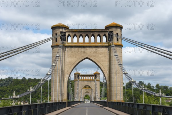 Historic bridge with distinctive arches and cables, surrounded by green landscape and a cloudy sky,