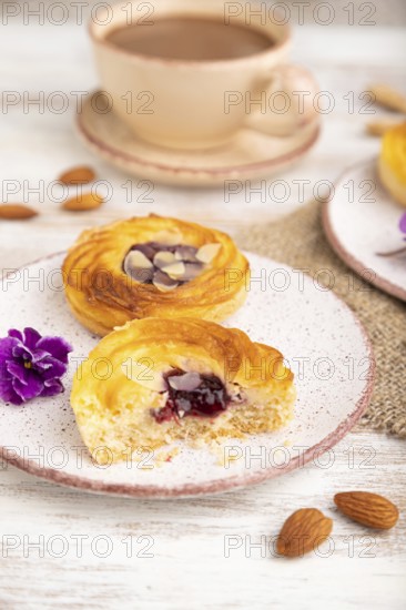 Small cheesecakes with jam and almonds with cup of coffee on a white wooden background and linen