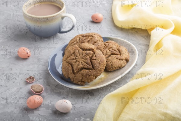 Homemade oatmeal cookies with a cup of cocoa and a yellow textile on a gray concrete background.