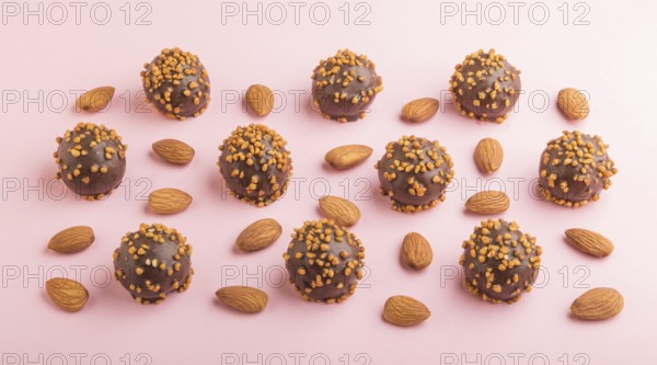 Chocolate caramel ball candies with almonds in a row on a pastel pink background. side view, close