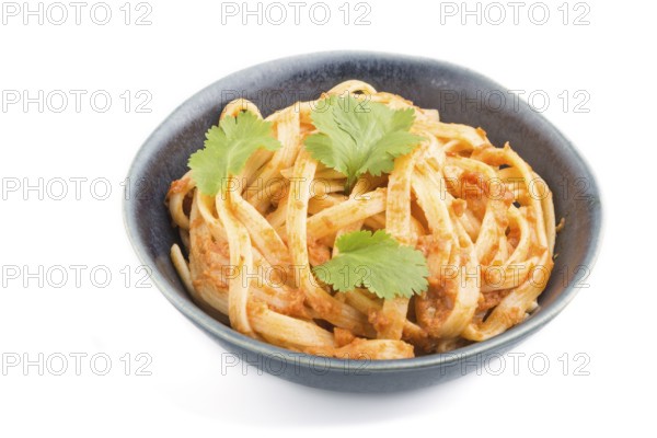 Semolina pasta with tomato pesto sauce, orange and herbs in bowl isolated on white background. Side