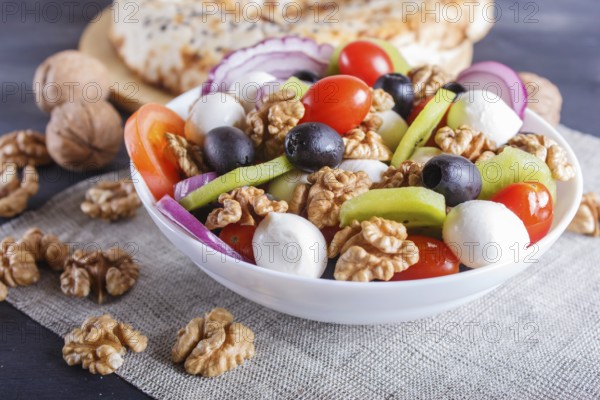 Salad with fresh cherry tomatoes, mozzarella cheese, black olives, kiwi, onion and walnuts on black