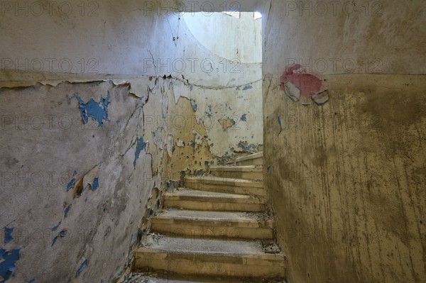 Dilapidated staircase with peeling paint and round window through which light enters, Lost Place,