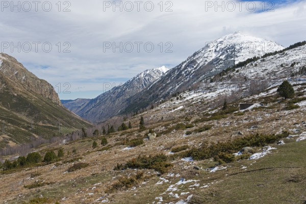 Gebirgstal mit teils schneebedeckten Gipfeln und winterlicher Landschaft unter bewölktem Himmel,