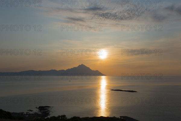 The sun rises, illuminating the sea and an island in the distance, view of Mount Athos, Orthodox