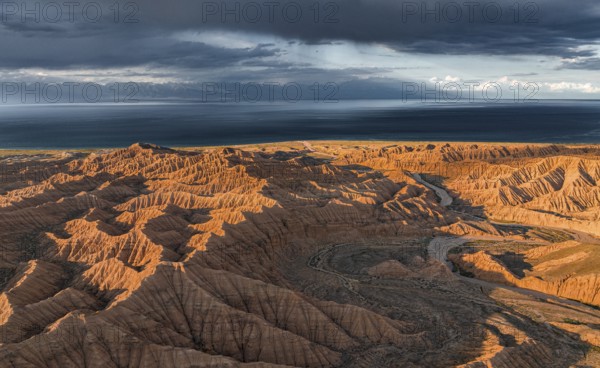 Riverbed runs through a landscape of eroded hills, badlands at sunset, Issyk Kul Lake in the