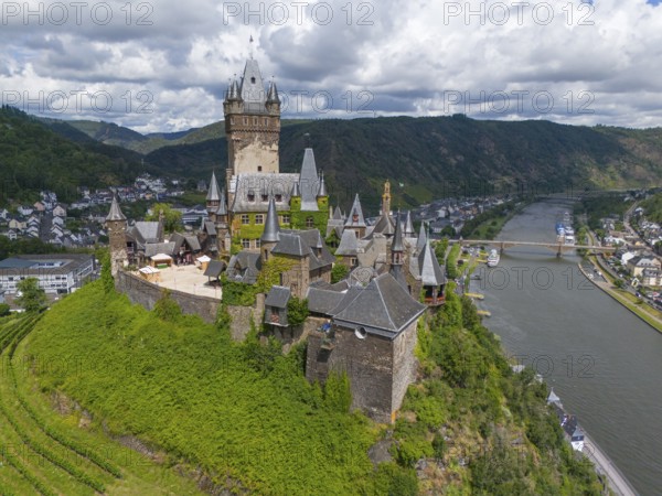 Medieval castle on a hill overlooking a river and a town, embedded in green nature and surrounded