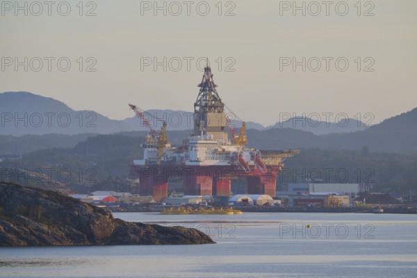 Oil rig in a calm seascape against a mountain backdrop in peaceful light, autumn, Bergen, North