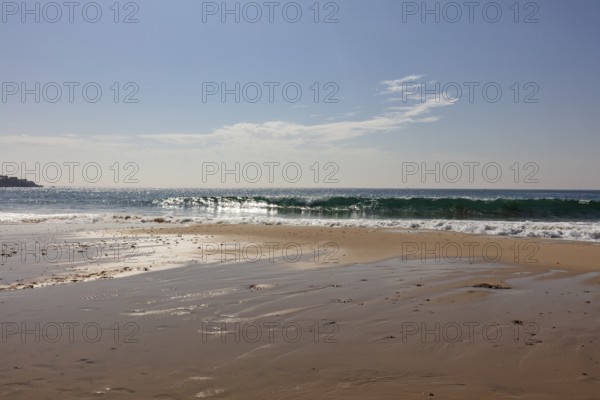 Breaking waves on a calm stretch of beach under a clear sky, Tarifa