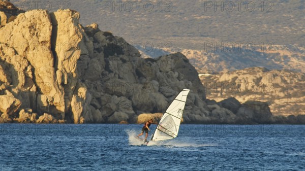 A windsurfer navigates past large rock formations, windsurfer, Meltemi windsurfing spot, Devils