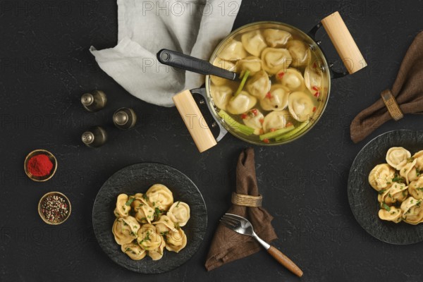 A pot filled with steaming dumplings sits on a dark textured surface. Two plates hold portions of