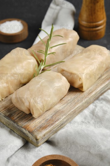 Close-up view of cabbage spring rolls stuffed with meat on a wooden board. A sprig of rosemary adds