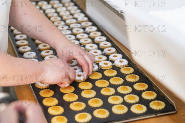 Two hands decorating double-layered round biscuits on a baking tray, Christmas baking, Black