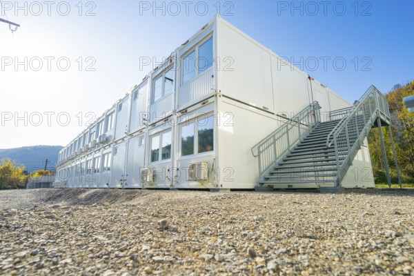 Container building with stairs, graphic lines in front of blue sky and nature, refugee