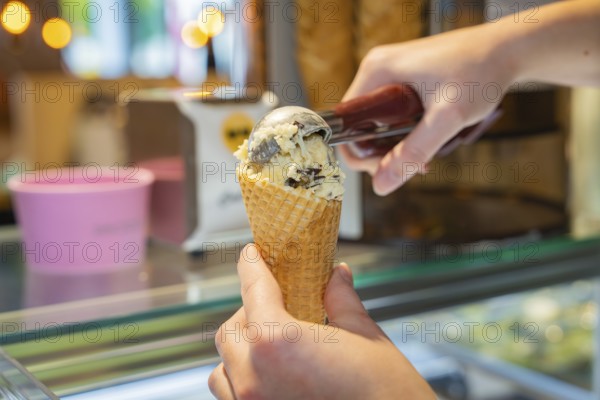 Vanilla ice cream with chocolate pieces is filled into a waffle with an ice cream scoop, autumn