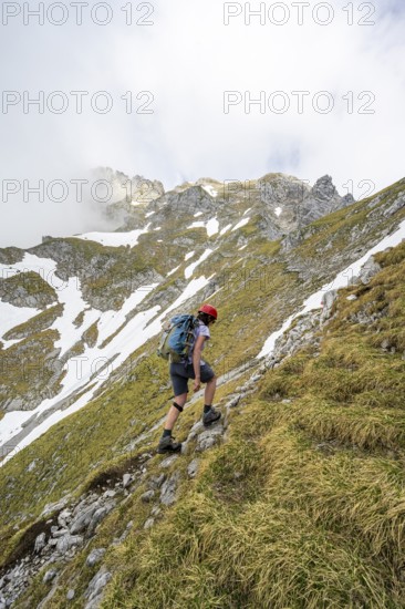 Mountaineer with helmet on a narrow hiking trail, ascent to the Ackerlspitze, clouds moving around
