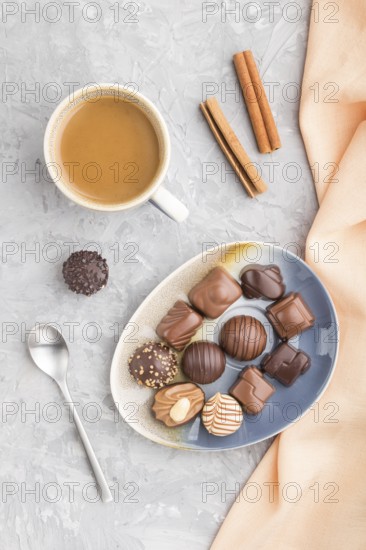 Different chocolate candies and a cup of coffee on a gray concrete background and orange textile.
