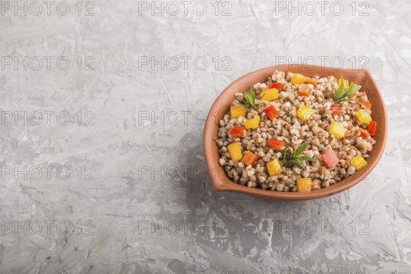 Buckwheat porridge with vegetables in clay bowl on a gray concrete background. Side view, copy