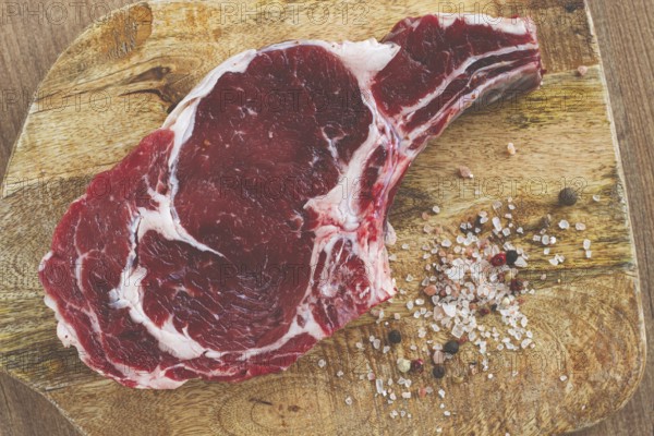 Raw rib eye steak, cowboy steak, on a wooden chopping board, top view, no people