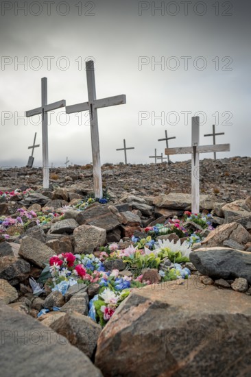 White crosses mark flower-decorated graves in a cemetery in foggy weather, remote Arctic Inuit