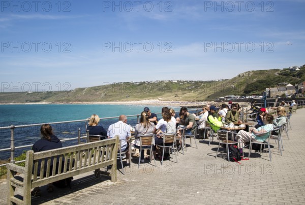 People sitting outdoors at cafe tables by the sea, Sennan Cove, Land's End, Cornwall, England, UK